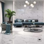 Modern living room with white marble walls and floor, a teal sectional, gray chair, large plant, and circular coffee tables.